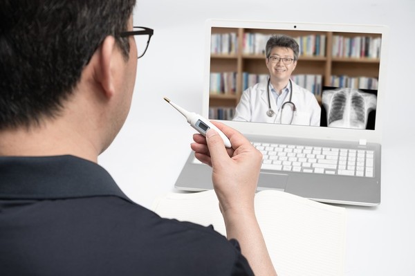 Man taking his own temperature while speaking with his doctor via his laptop.