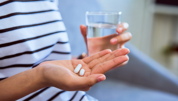 Person holding two pills and glass of water